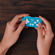 The 8BitDo Zero 2 controller in blue being held in two hands over a wooden table.